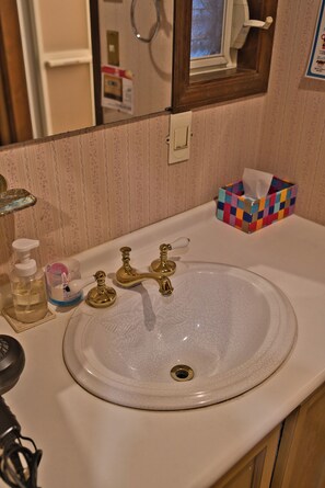 A bathroom with a white sink, gold faucets, a mirror, and a colorful tissue box. - Iza Kamakura Guest House & Bar - Hostel (Kamakura)