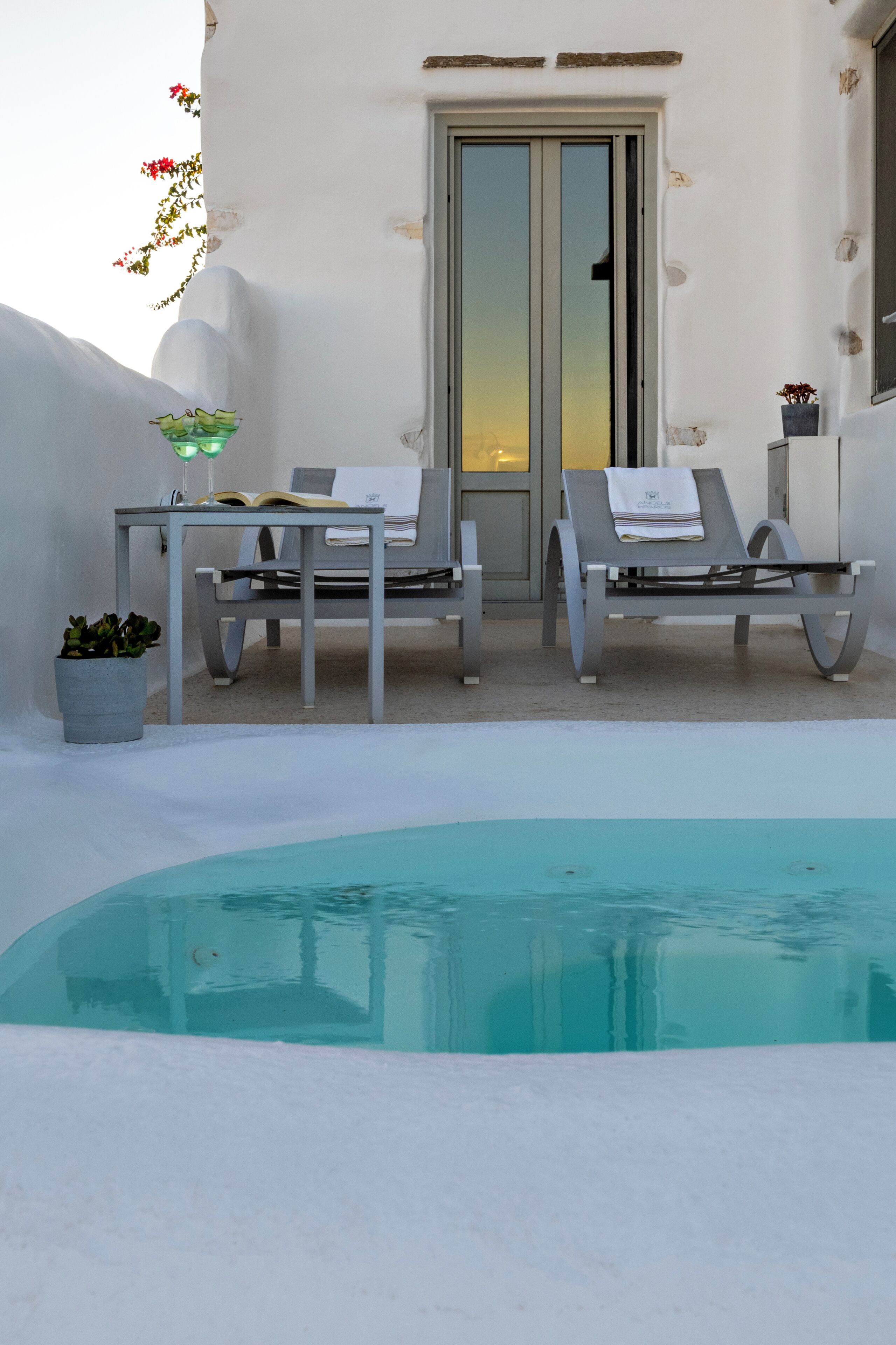 A poolside area with two lounge chairs, a table with a book and a lamp, and a potted plant.
