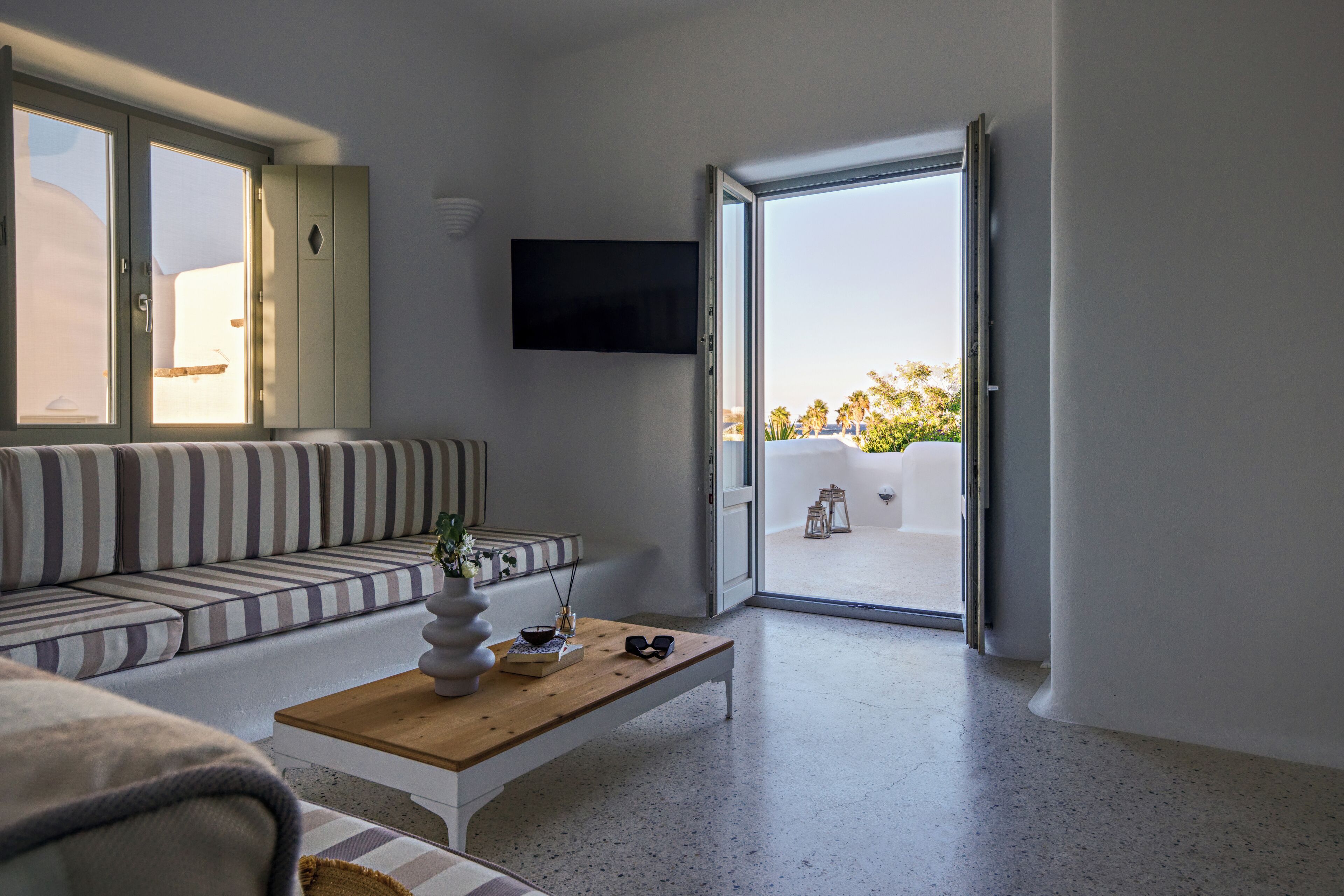 A modern living room with a sofa, a coffee table, a flat-screen TV, and a sliding glass door leading to an outdoor balcony.