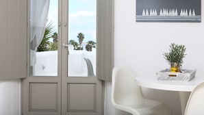 A room with a sliding glass door leading to a balcony, a white table with a plant, and a framed picture on the wall. - Angels Villas (Paros)