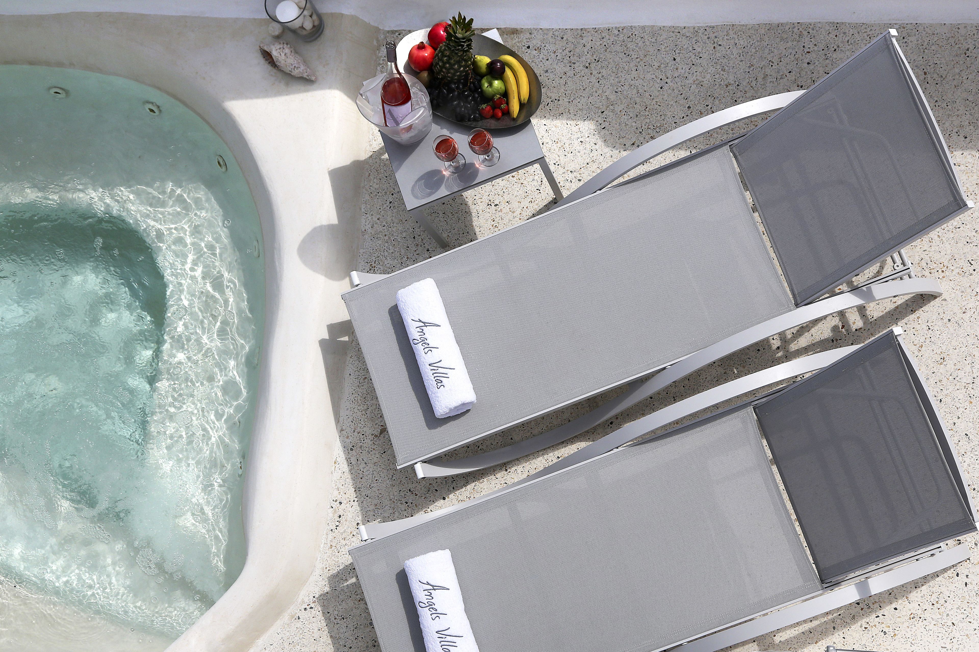 A poolside area with two lounge chairs, a table with fruits and drinks, and a hot tub.