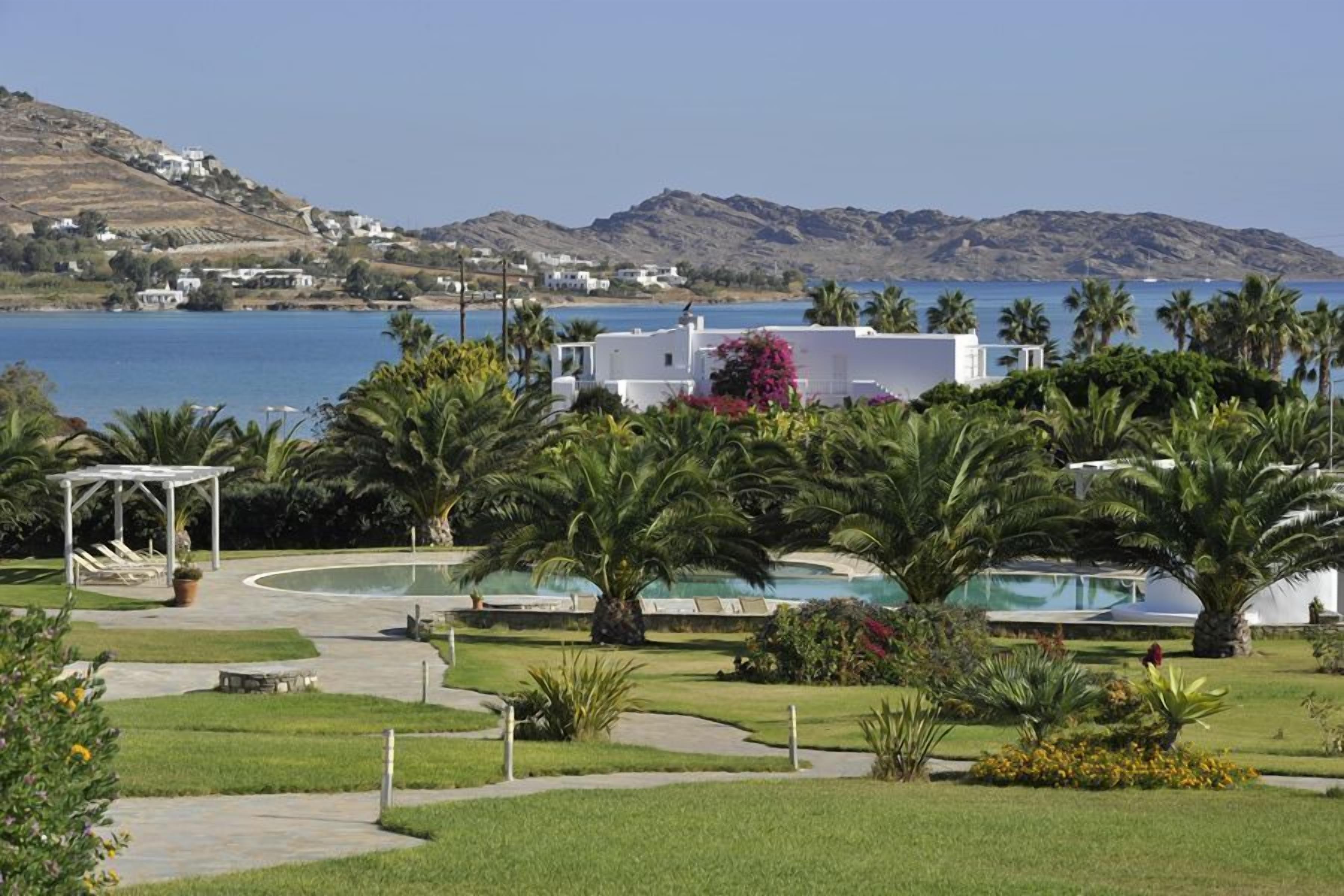A resort with a pool area, palm trees, and a view of the sea and hills.