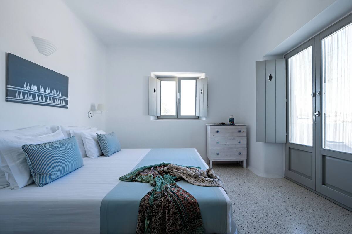 A bedroom with a bed, a dresser, a window, and a painting on the wall.