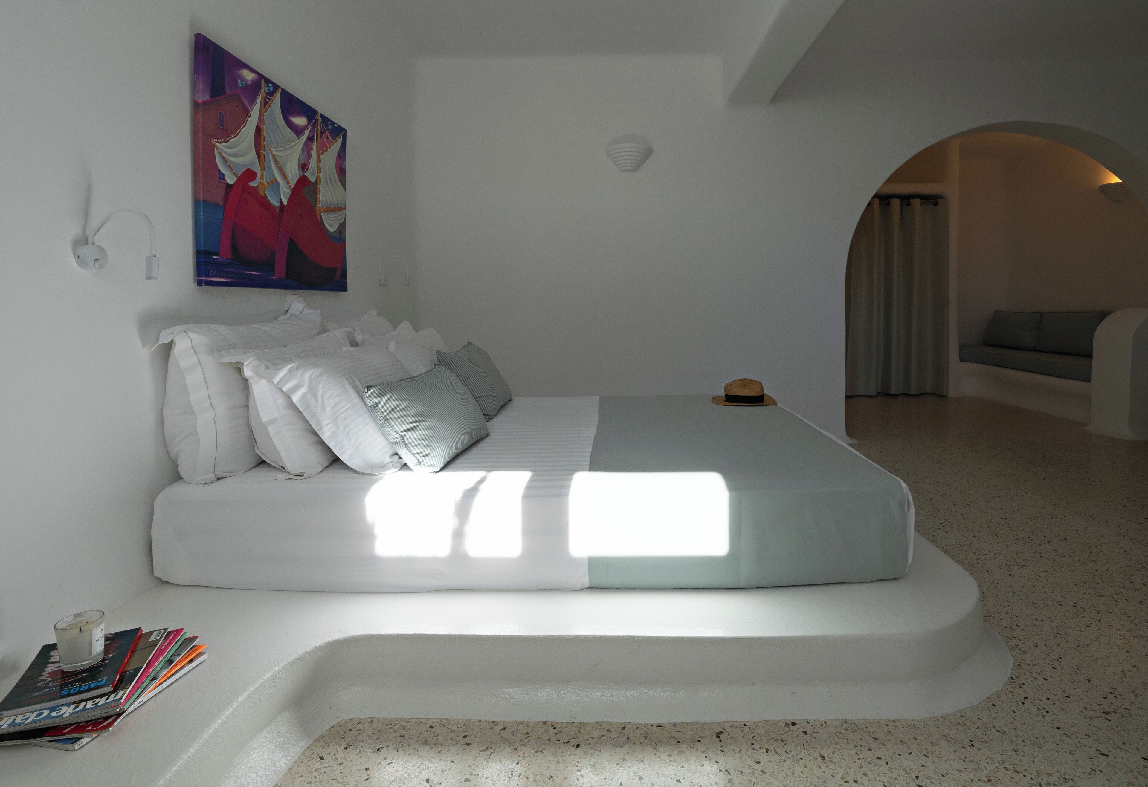 A modern bedroom with a curved bed, white bedding, and a painting above the bed.