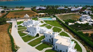 An aerial view of a coastal residential area with white buildings, a swimming pool, and a clear view of the sea. - Angels Villas (Paros)