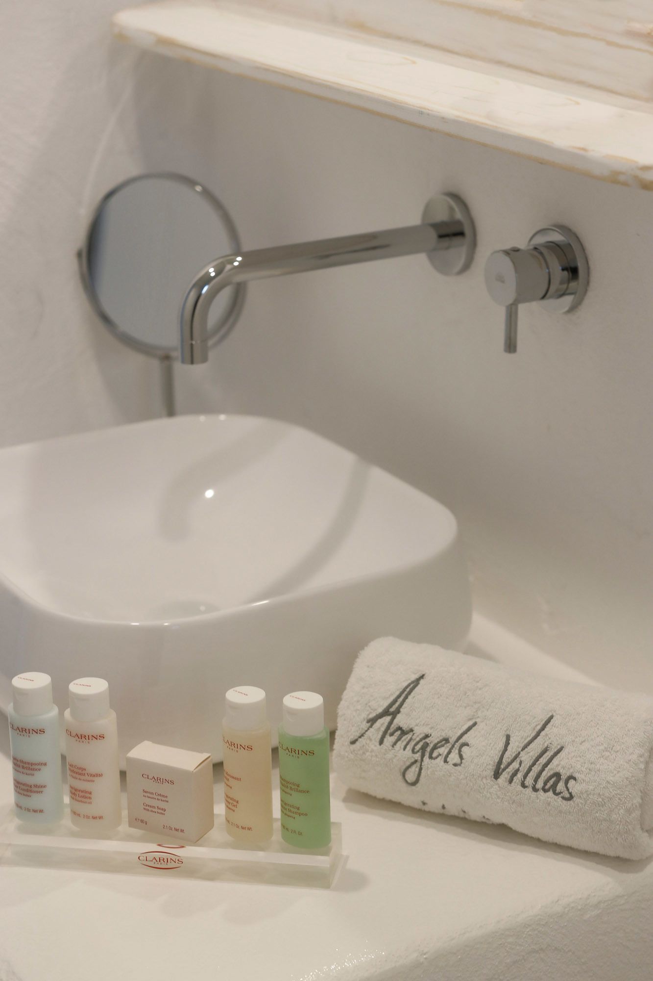 A bathroom with a white toilet, a round mirror, a towel rack, and toiletries including Clarins products.