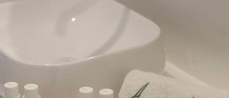 A bathroom with a white toilet, a round mirror, a towel rack, and toiletries including Clarins products.