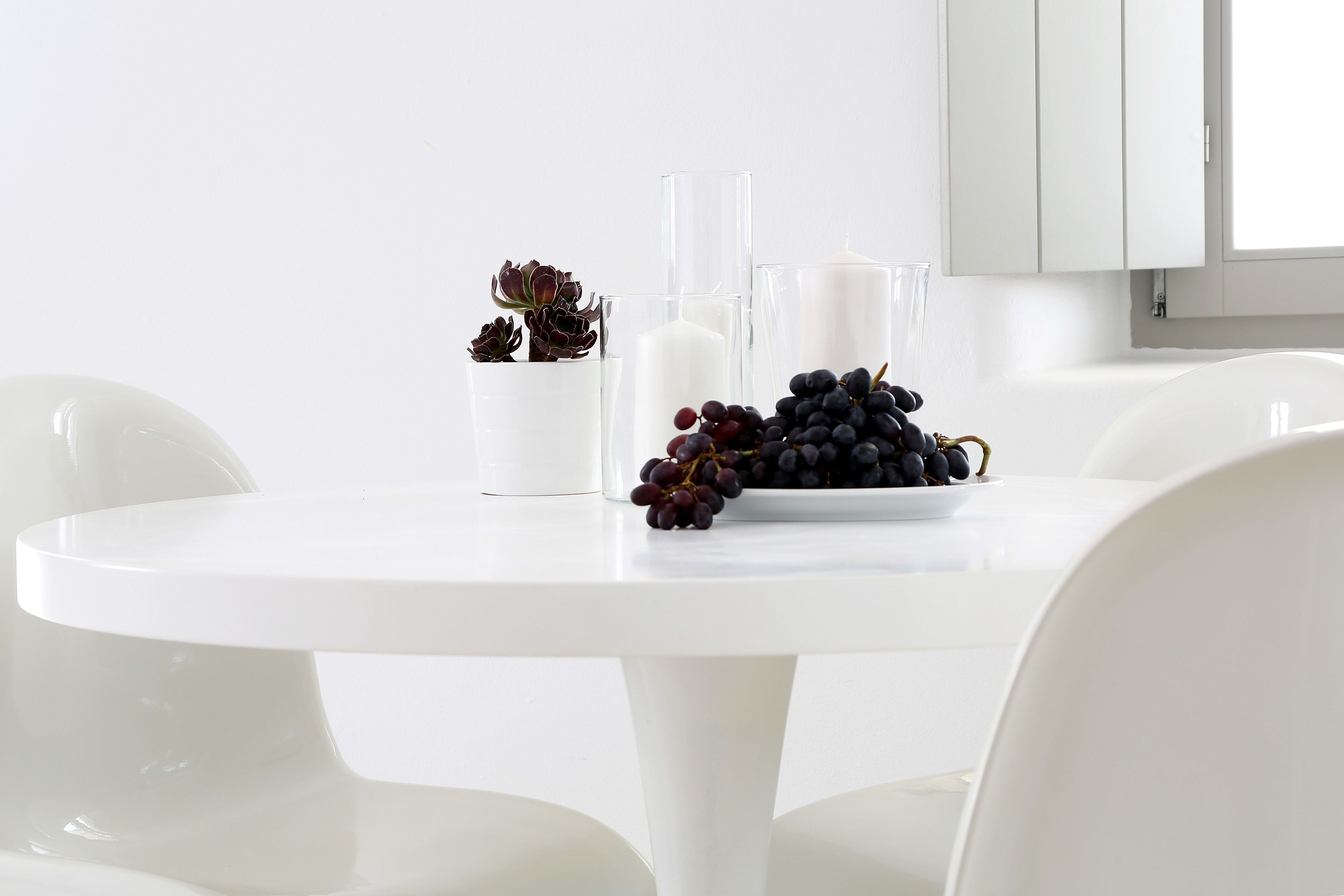 Una mesa blanca con un florero de suculentas, un vaso de leche y un plato de uvas.