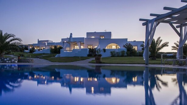 A modern resort with a reflective pool, white buildings, and palm trees. - Angels Villas (Paros)