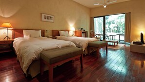 A hotel room with two beds, a wooden floor, a desk, a chair, and a large window with a view of greenery. - Forest Village (Fujikawaguchiko)