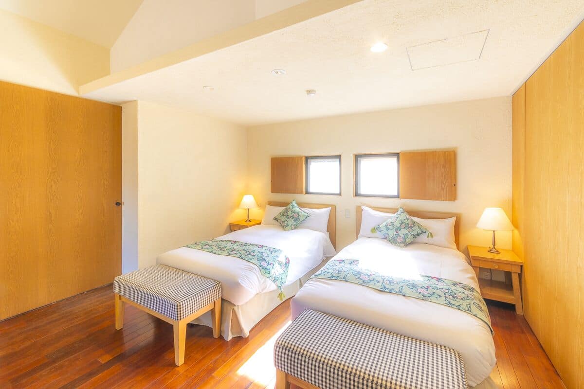 A hotel room with two beds, wooden flooring, and a small bench.