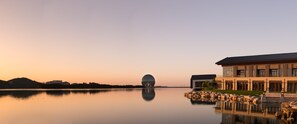 A modern building with a spherical structure in the background, a calm body of water reflecting the building, and a clear sky. - Yanqi Hotel (Huairou)