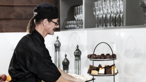 A person serving desserts from a three-tiered stand in a kitchen with a white tiled backsplash and decorative metal candle holders. - Kings Park (Chinchilla)