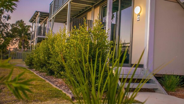 A modern building with a balcony, a well-maintained garden, and a lit entrance sign. - Kings Park (Chinchilla)