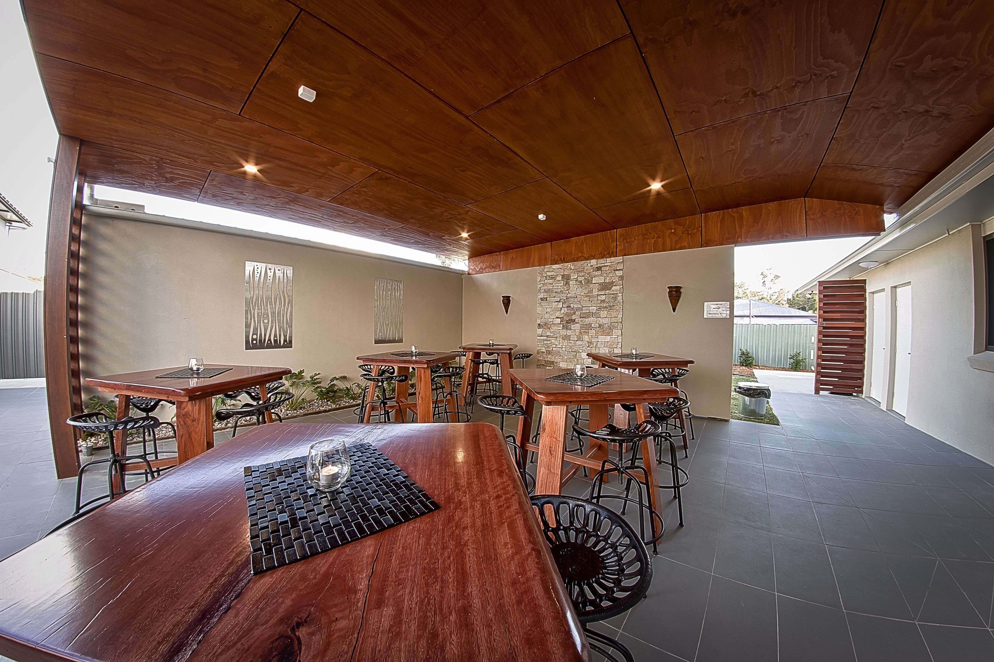 Un espace de restauration en plein air avec plusieurs tables et chaises en bois, un mur en pierre et un plafond en bois.