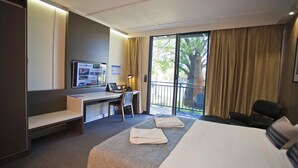A hotel room with a bed, a desk, a chair, a TV, and a balcony with curtains. - Kings Park (Chinchilla)