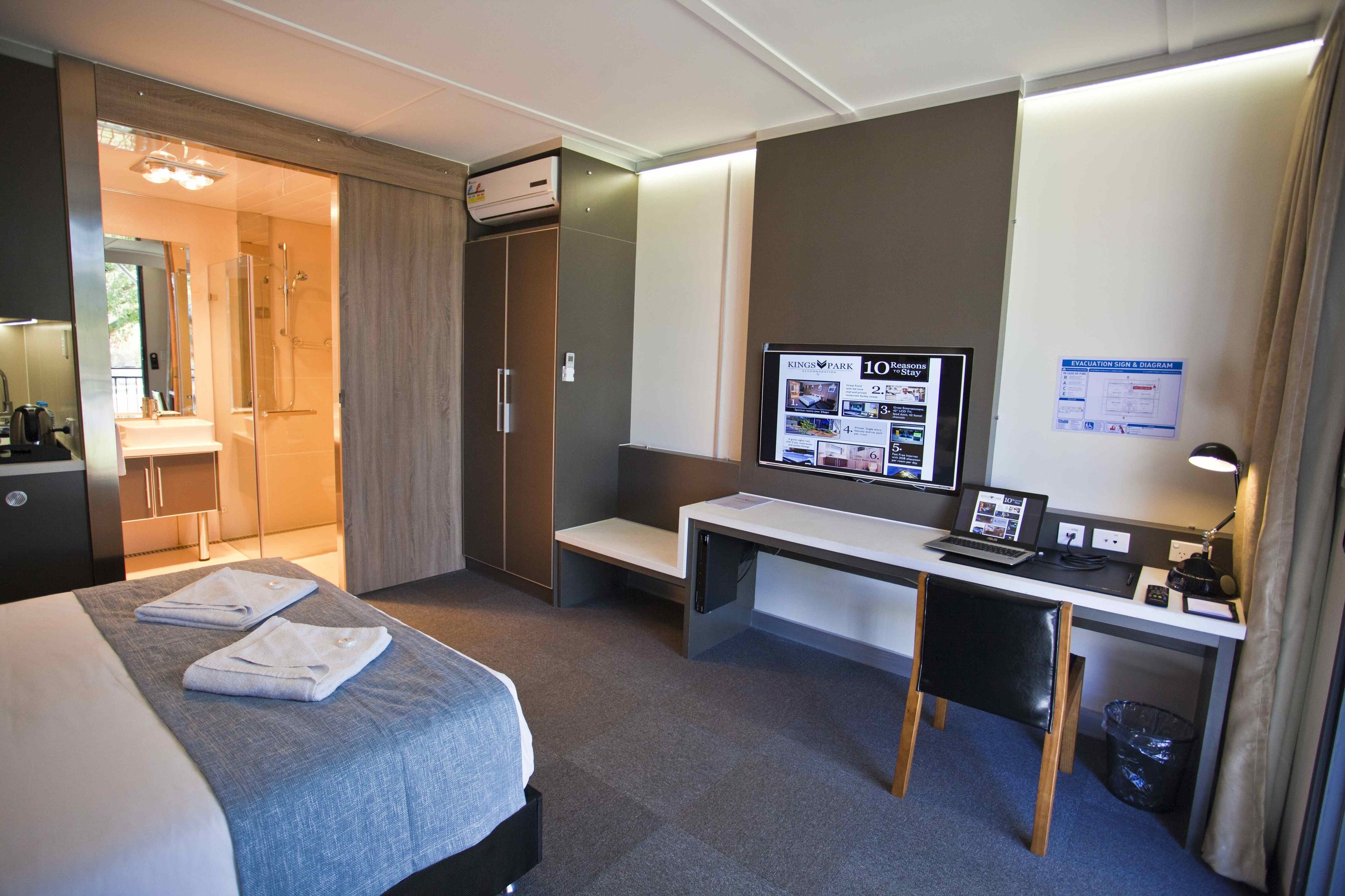 A hotel room with a bed, a desk, a computer, and a TV.