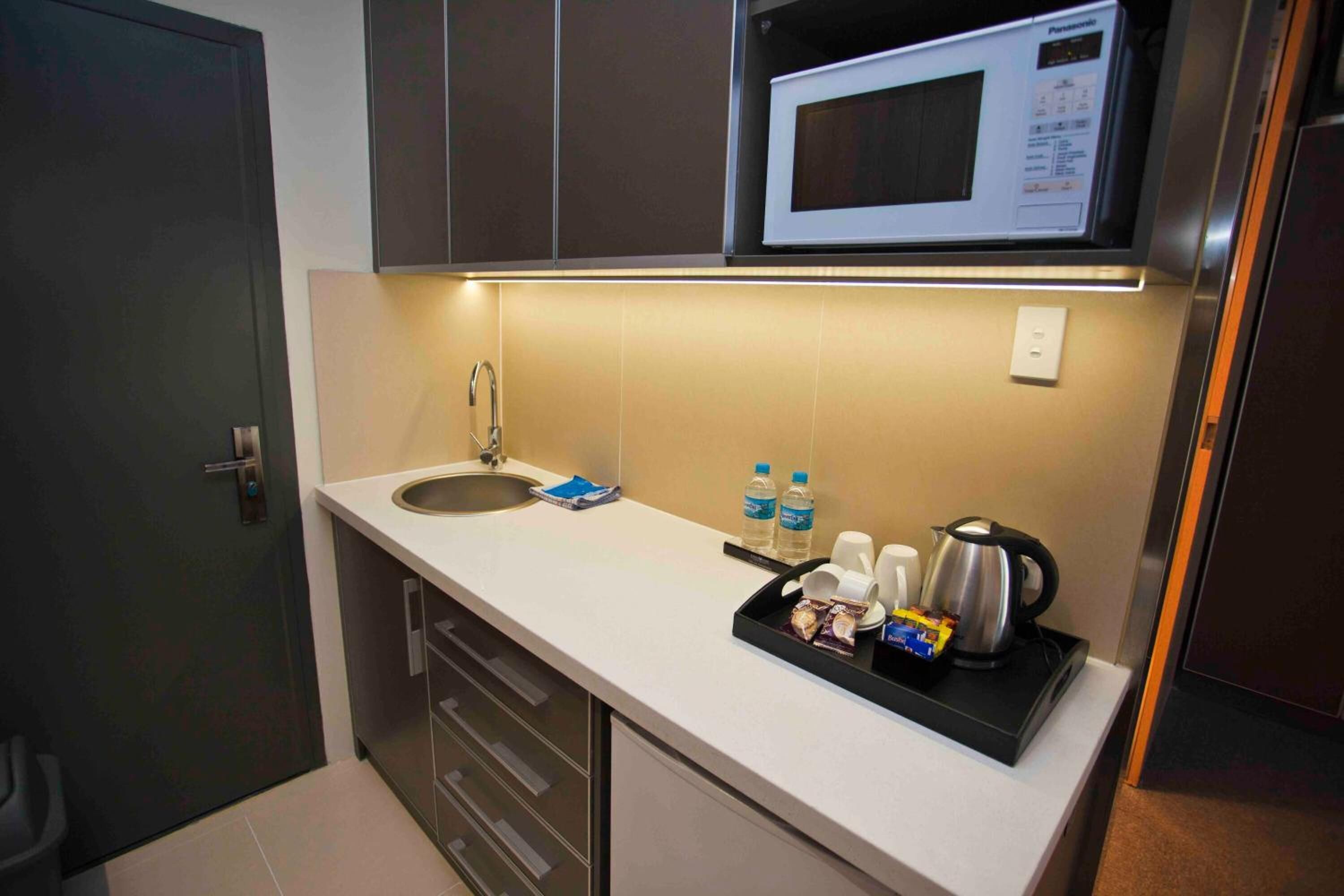 A compact kitchen with a microwave, sink, and a tray with snacks and a kettle.