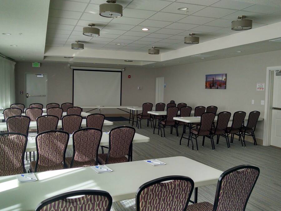 A conference room with tables and chairs, a projector screen, and an exit sign.