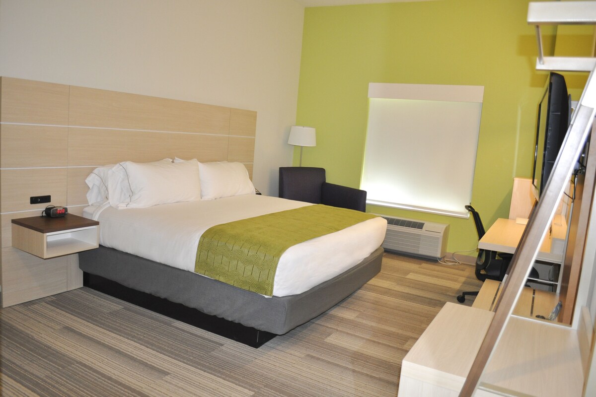 A hotel room with a bed, bedside table, lamp, and a large window.