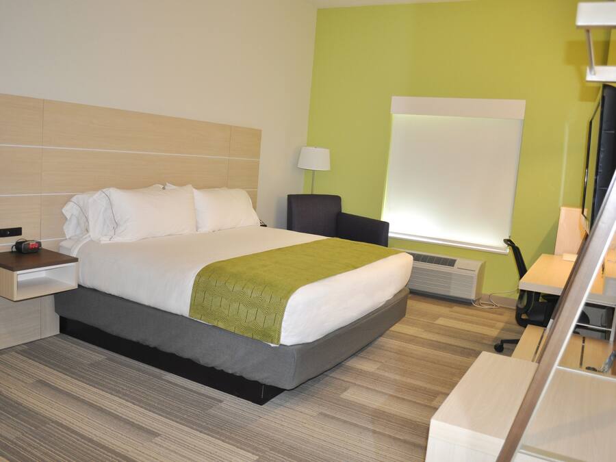 A hotel room with a bed, bedside table, lamp, and a large window.