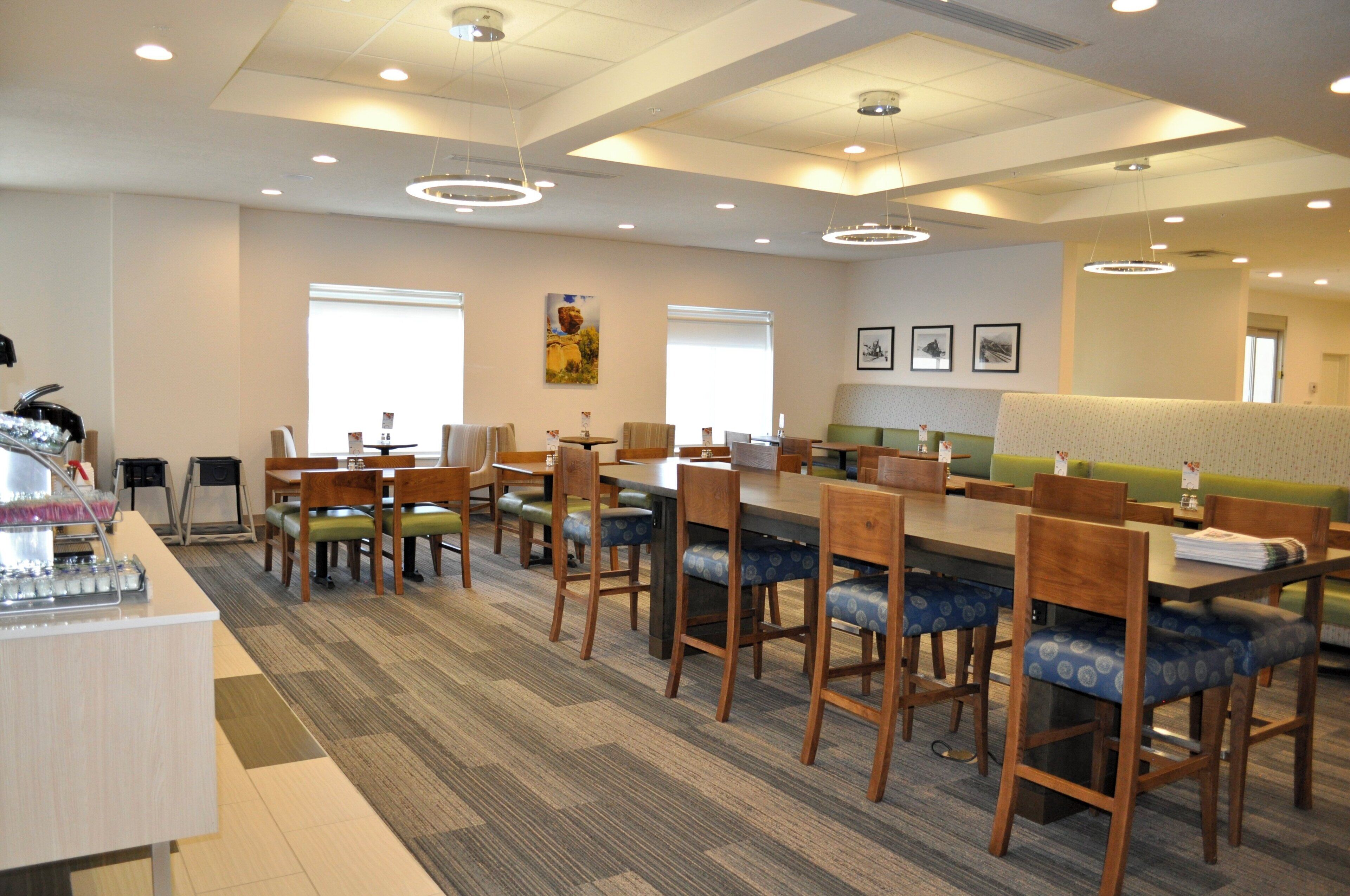 Un grand espace dédié à la salle à manger, avec plusieurs tables et chaises, un comptoir doté d’un distributeur de boissons et un mur orné de tableaux.