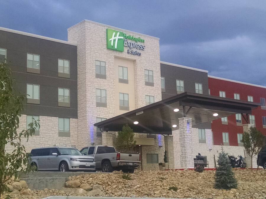 Edificio de Holiday Inn Express & Suites con un acceso cubierto y varios vehículos estacionados al frente.