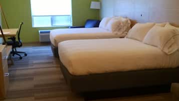 Habitación de hotel con dos camas, un escritorio, una silla, una lámpara y una ventana con persianas.