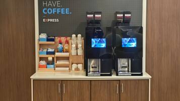 Una estación de café con dos máquinas de café, un letrero que dice “MUST HAVE COFFEE”, y diversos artículos relacionados con el café en estantes.