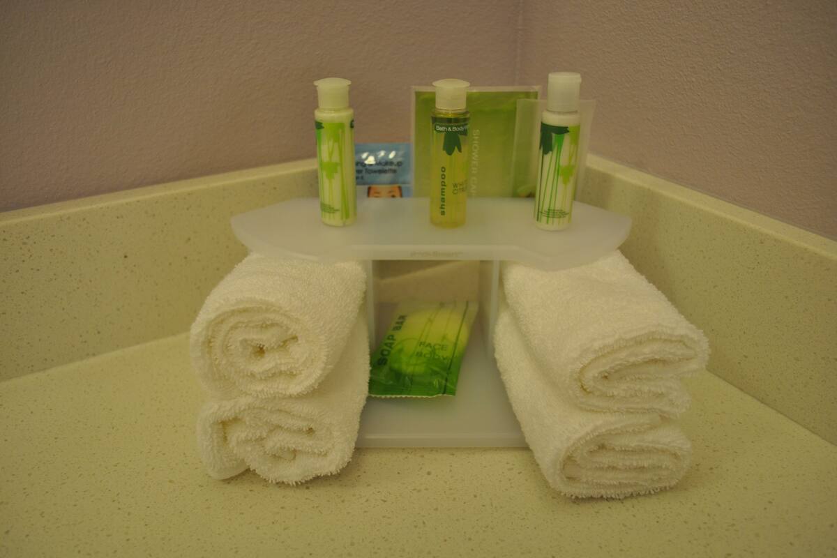 A bathroom with a white sink, two rolled white towels, and three green bottles of soap on the sink.