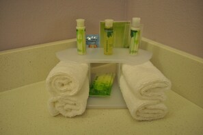 Une salle de bain avec un lavabo blanc, deux serviettes blanches roulées et trois bouteilles de savon vertes posées sur le lavabo.