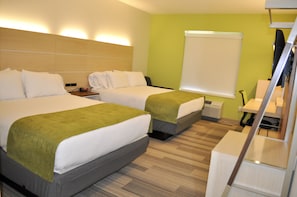 A hotel room with two beds, a desk, a chair, and a large window with a white blind.