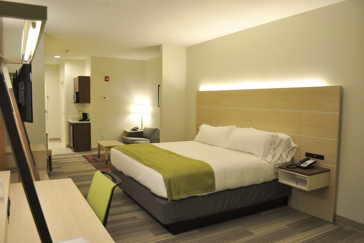 A hotel room with a bed, bedside table, lamp, and a desk with a chair.