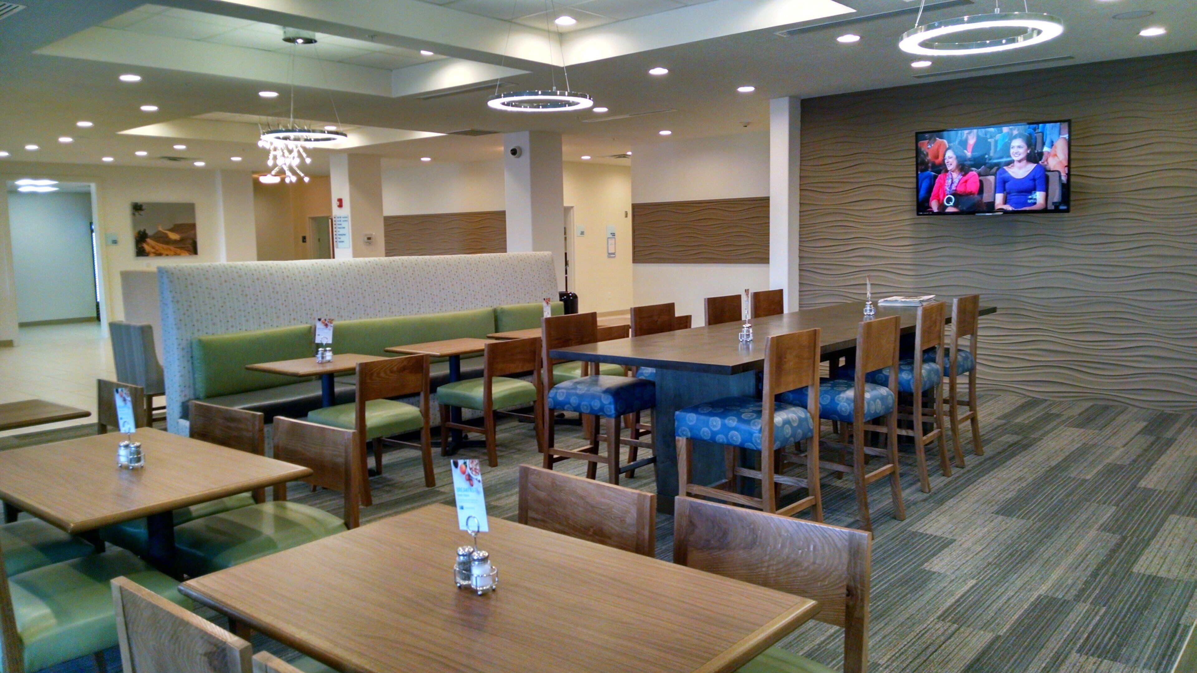 A hotel dining area with booths, tables, and a television screen displaying a program.