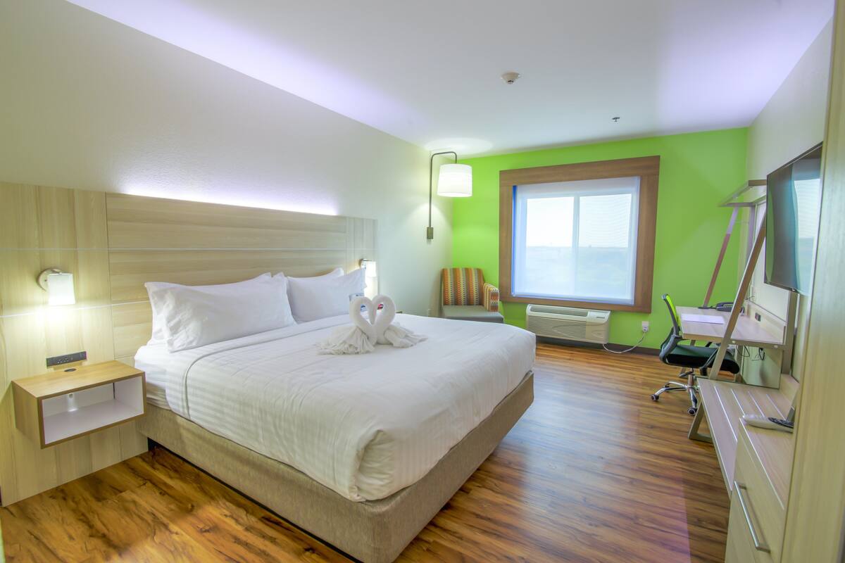 A hotel room with a large bed, a desk with a chair, a window, and a wall-mounted TV.