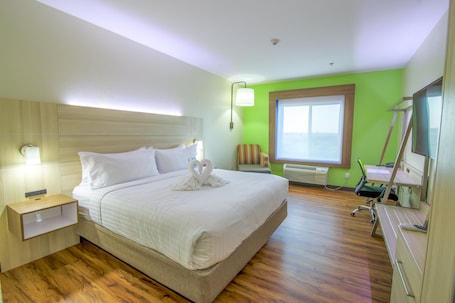 A hotel room with a large bed, a desk with a chair, a window, and a wall-mounted TV.
