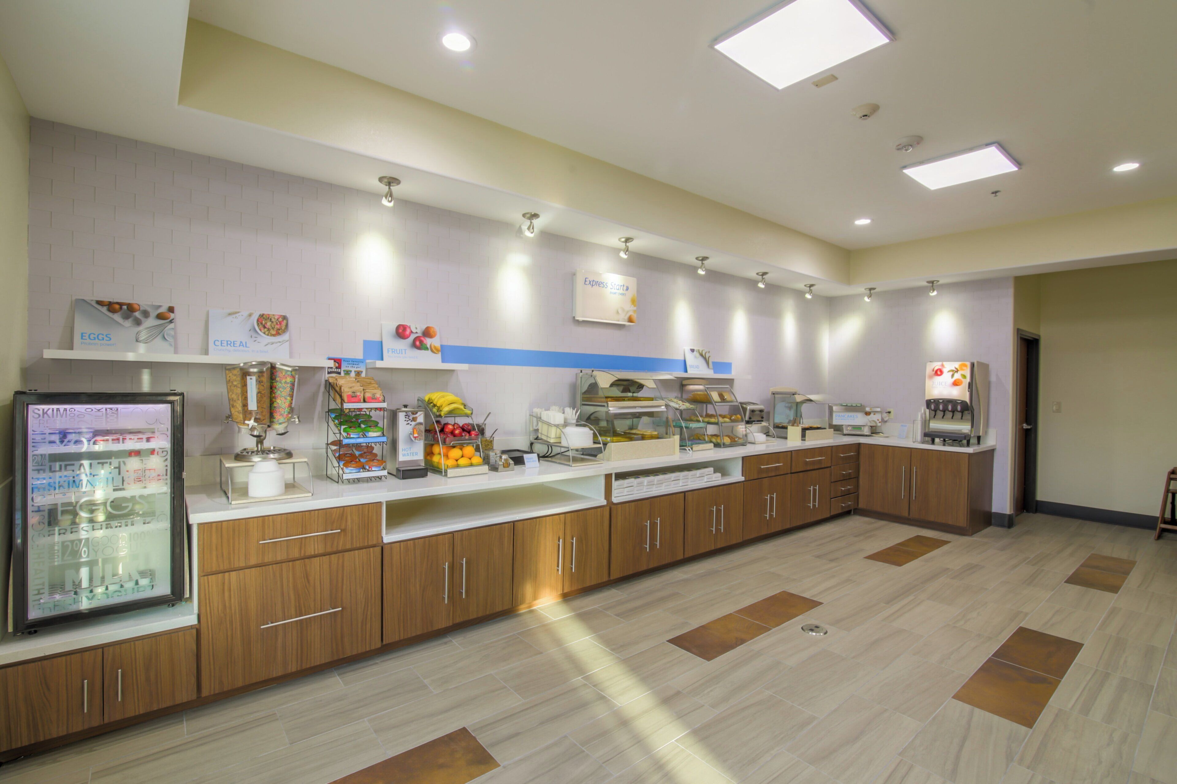 A self-service breakfast area with a refrigerated display, hot water station, and various food items.
