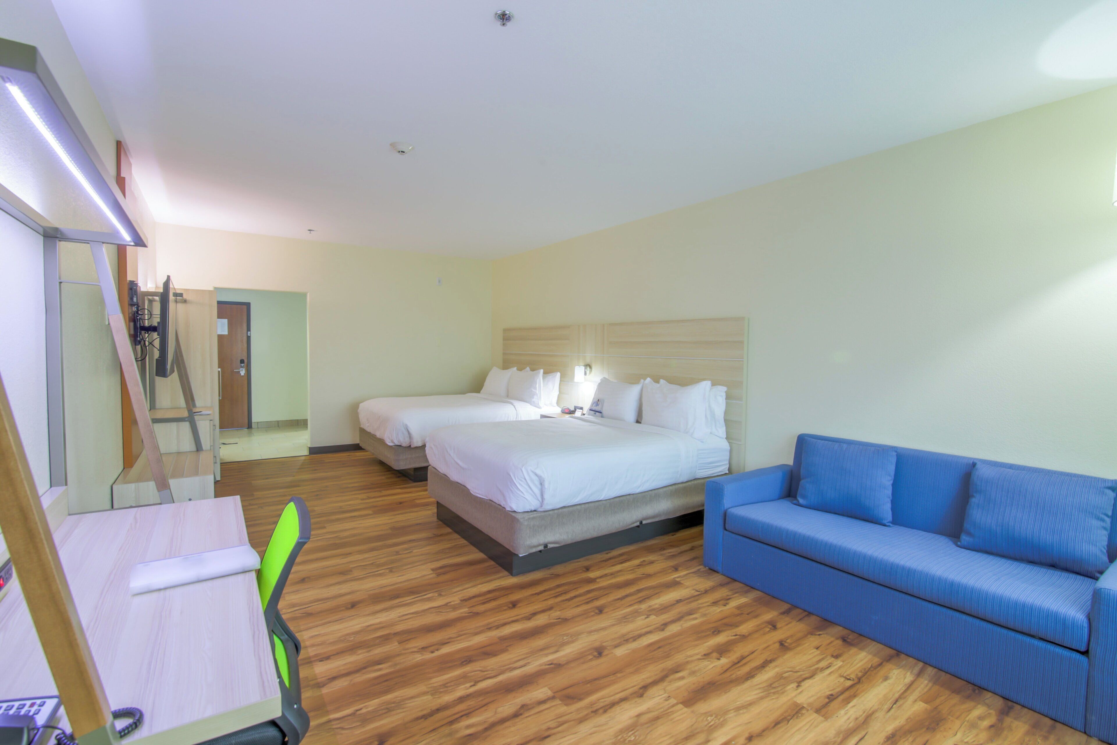 A hotel room with a bed, a blue sofa, a desk with a chair, and a wooden floor.
