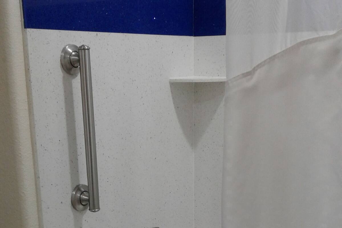 A bathroom with a white sink, a handheld showerhead, and a grab bar.
