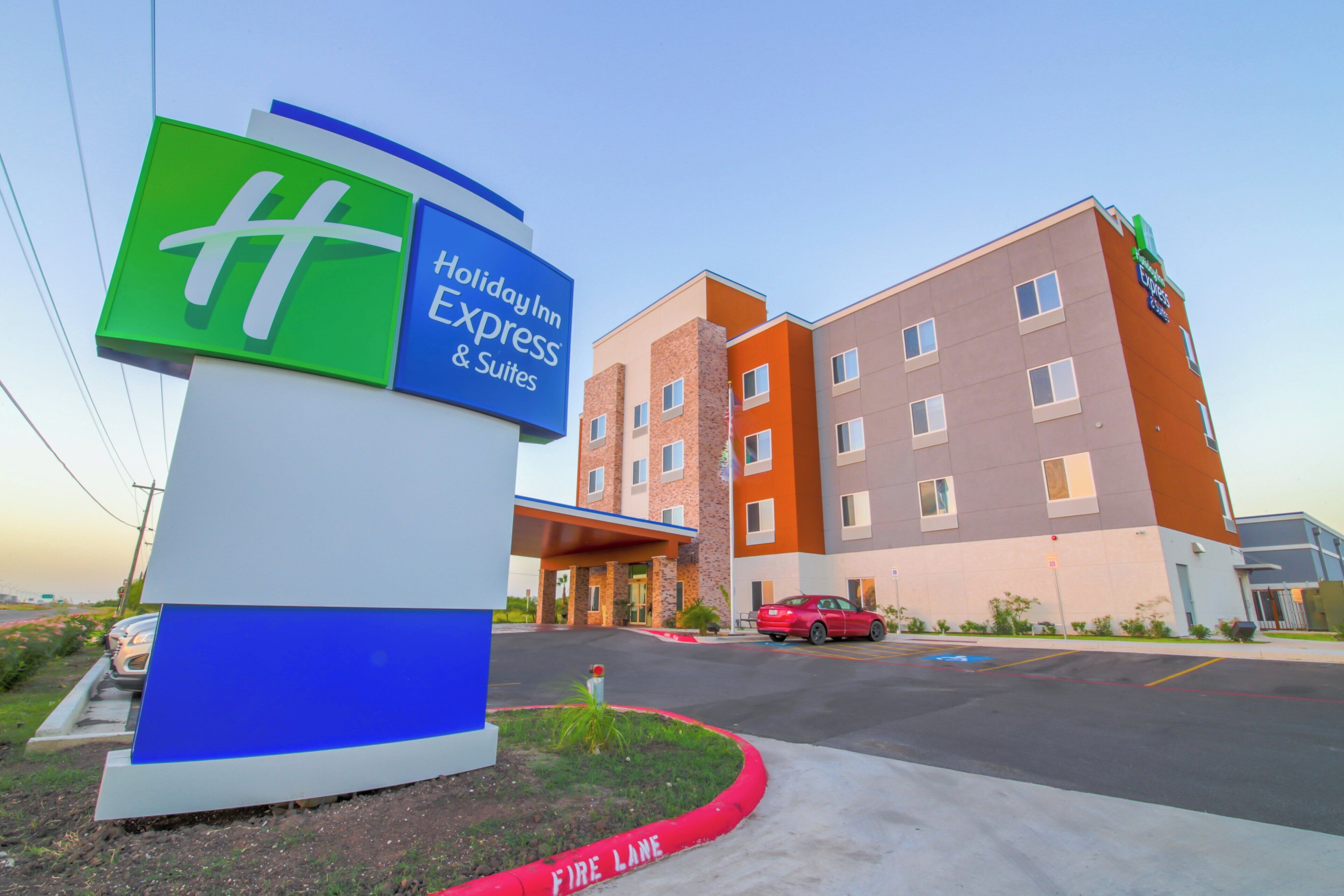 A Holiday Inn Express & Suites hotel with a prominent sign, a parking lot, and a red fire lane curb.