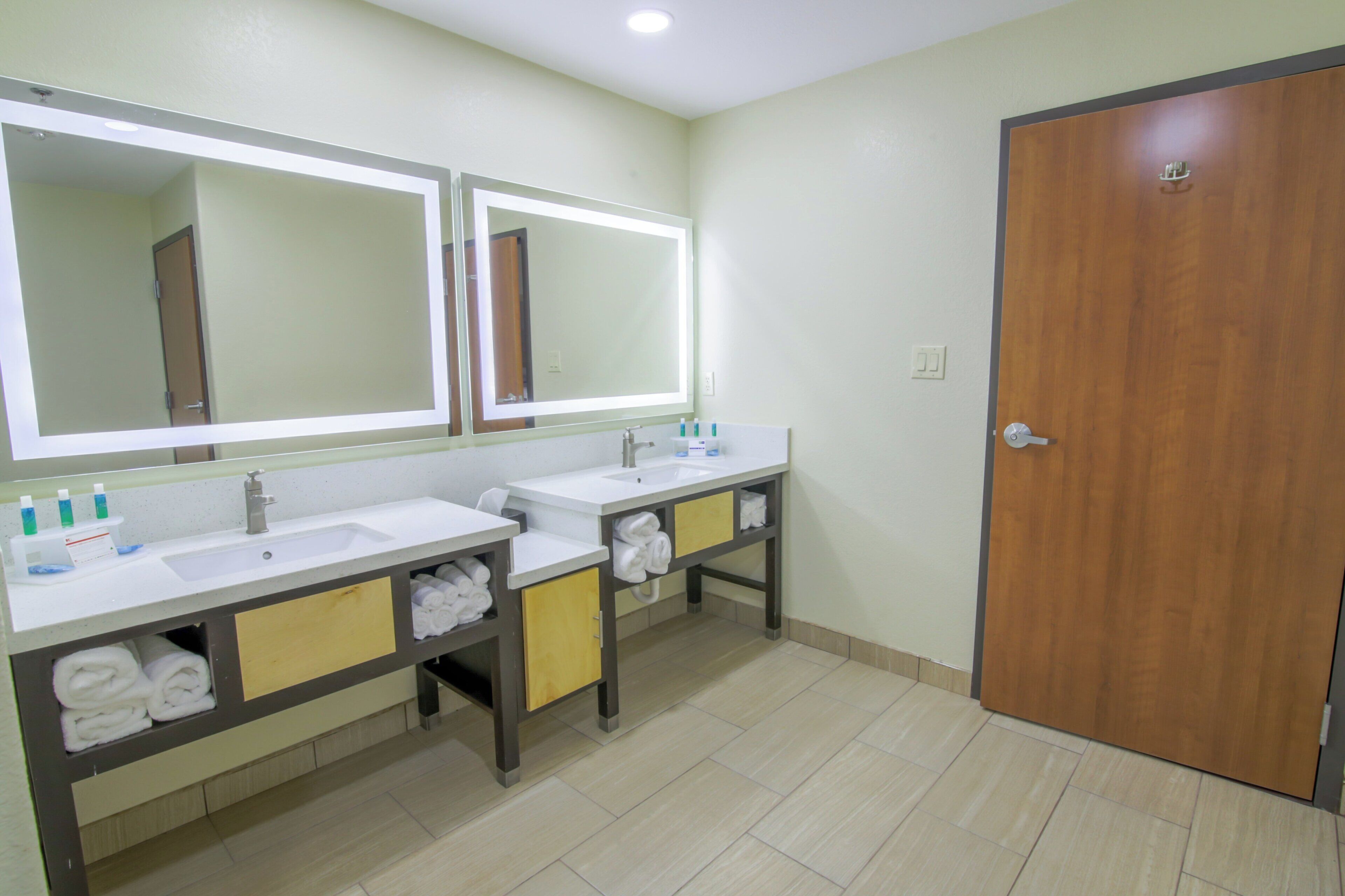 Un baño con dos lavamanos, un espejo y una puerta de madera.