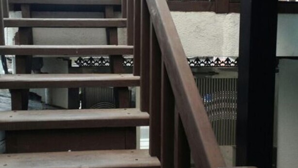 A wooden staircase with a metal railing, leading to an outdoor area with a fence and a building in the background. - Again Seoul Guesthouse (Seoul)