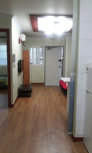Una habitación con suelo de madera, un televisor montado en la pared, una puerta con cortina y una pequeña mesa.
