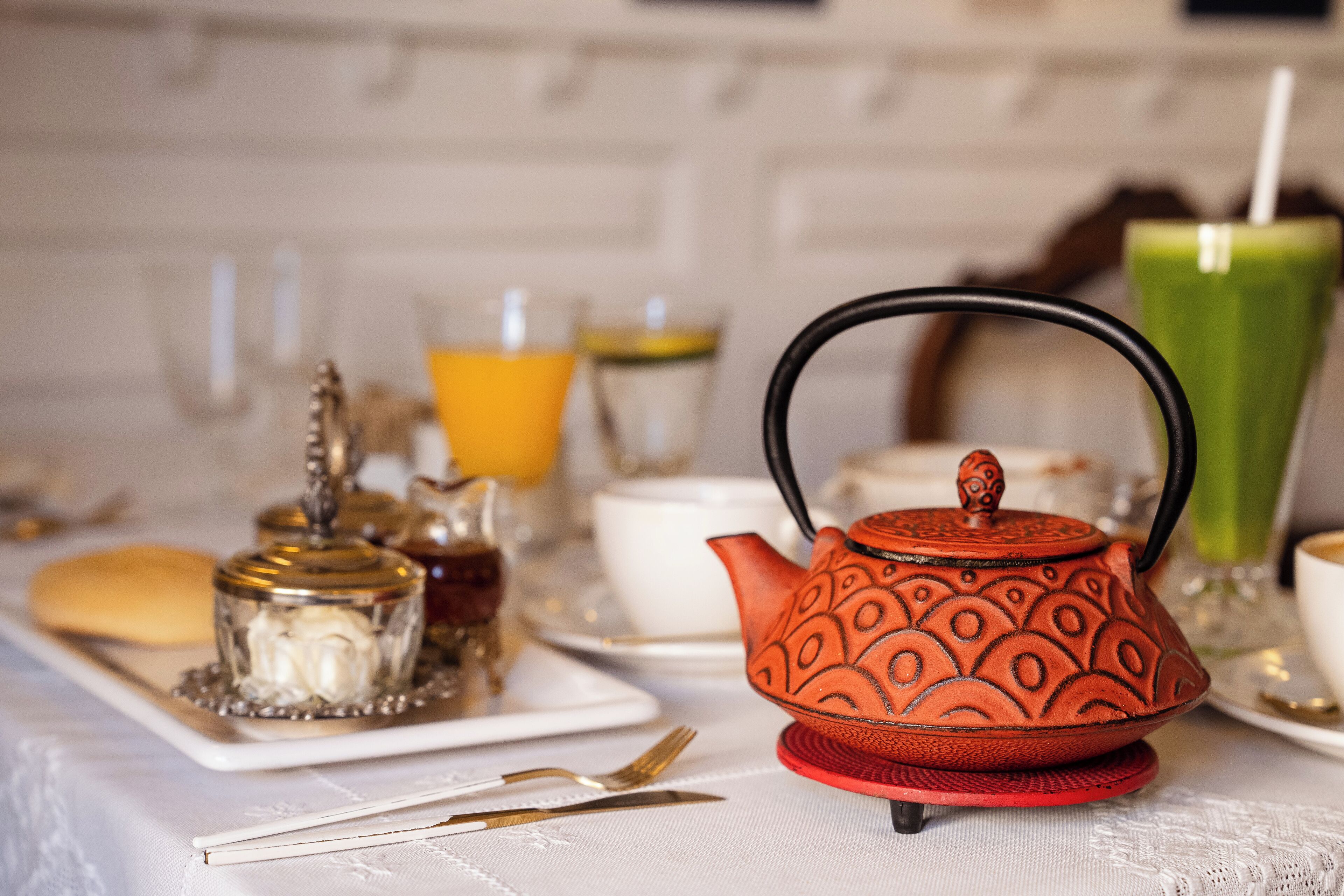 A table set with a teapot, cups, and a glass of green juice.