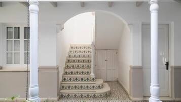 A staircase with patterned tiles leading to a door, surrounded by white columns and a tiled floor.