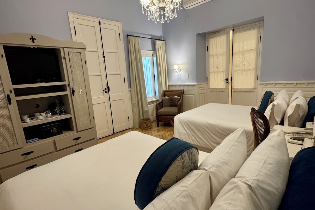 A hotel room with two beds, a wardrobe, a chandelier, and a window with curtains.