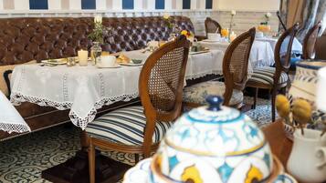 Zona pranzo con pareti a righe, un divano in pelle marrone, sedie di legno e un tavolo apparecchiato con piatti, bicchieri e un vaso decorativo.