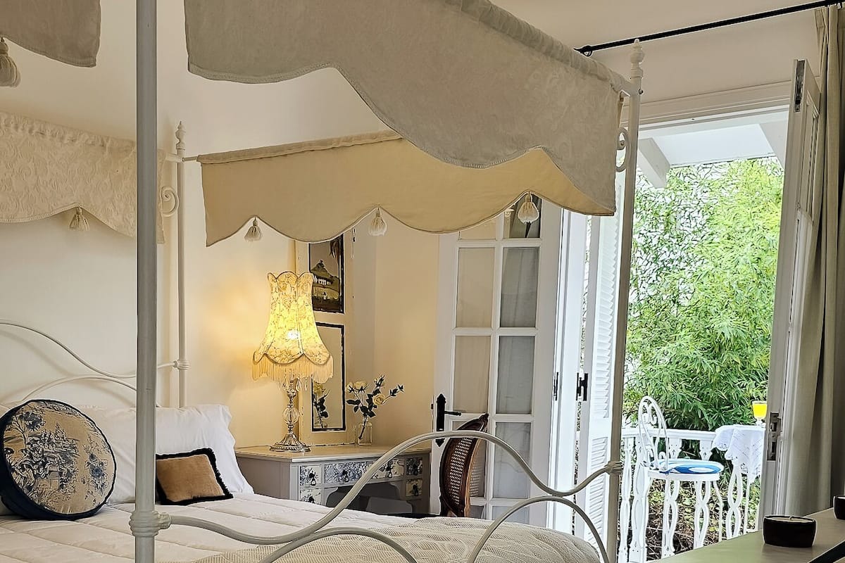 A four-poster bed with a canopy, a checkered floor, and a view of greenery outside.