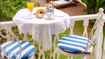 A white outdoor seating area with a table set for breakfast, including a croissant, orange juice, and a teapot.
