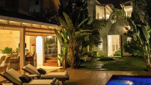 A pool area with lounge chairs, a wooden deck, and a building with a glass door. - Villa Vicuña Hotel Boutique (Salta)